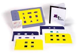 Blue, white, and yellow keyboard overlays on a flat surface, and behind that is a software disk leaning against an upright overlay and to the left is an open manual.