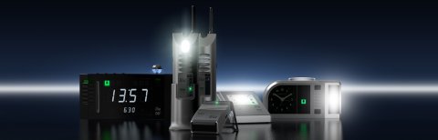 A black alarm clock with a lisa receiver on top, two silver RF repeaters with black antennas, a silver portable receiver, a table-top blinking lamp, and an analog clock with a bright light attached to the right.