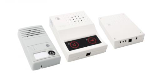 Three white rectangular boxes. The first, the door unit, includes a speaker at the top and a screen with a doorbell icon below. The second, the room unit, includes a speaker at the top and a  lack screen below with icons for speaking and for a key. The last object is the central unit, which includes a single port on the bottom.