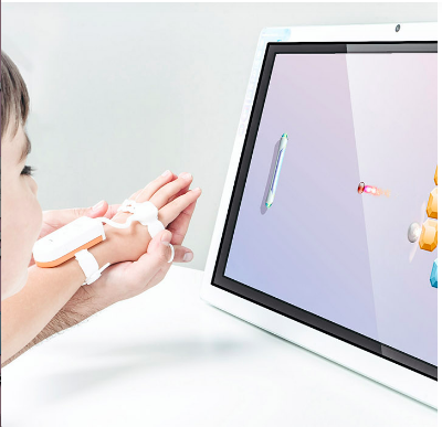 A partial shot of a small child viewing a screen. The child's arm is extended and the hand is supported in a larger person's hand. On the back of the wrist and knuckles are straps and a white rectangular device.