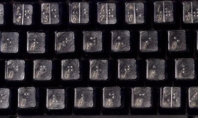 A close-up of a standard black keyboard with Braille lettering in place of standard lettering. The sticker overlay is printed on translucent material, so the black keys are still visible. 