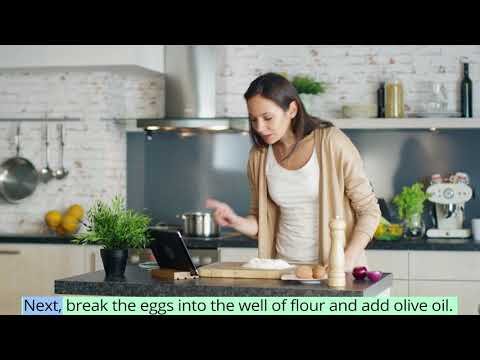 A woman at a kitchen counter looking at her laptop and pointing.