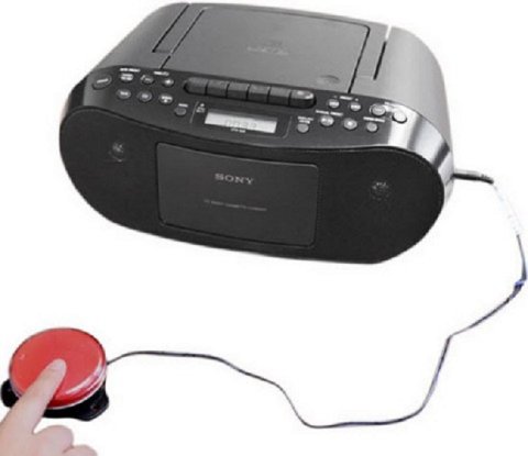 Black boom box with switch and cable extending from side with red switch device attached to end and finger pressing switch button.