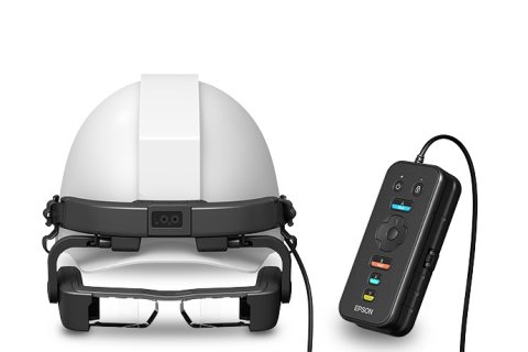 Wearable device resembling a pair of narrow goggles. They are shown fitted beneath an industrial safety helmet. The device is medium-grey in color. Also shown is a medium-sized, rectangular, and black device that is attached to the glasses by a cord.