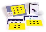Blue, white, and yellow keyboard overlays on a flat surface, and behind that is a software disk leaning against an upright overlay and to the left is an open manual.
