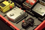 Image of several guitar and bass pedals next to a small, rectangular, and black device.