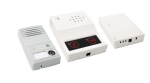 Three white rectangular boxes. The first, the door unit, includes a speaker at the top and a screen with a doorbell icon below. The second, the room unit, includes a speaker at the top and a  lack screen below with icons for speaking and for a key. The last object is the central unit, which includes a single port on the bottom.