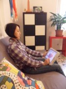 Picture of a woman sitting on a couch holding a tablet PC on her lap with her left hand and pointing to the screen with her right hand.