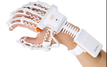 A human's hand that has a white skeletal-type device on it, extending down the back of each finger and ending below the wrist. There is a small rectangular compartment on the back below the wrist and the knuckles.