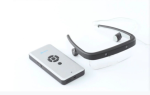 A small rectangular device, about the size of a smartphone with a circular layout of 4 buttons and with another button in the middle of these 4 and one below them. Next to this device are a specialized pair of glasses with a black frame that has 2 small recessed cameras spaced apart on the front and 2 small round cylinders where the ears would be. The glasses are resting on a single clear front lens that has a notch for the nose bridge.