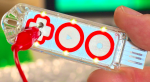 A plastic object that looks like a USB flash drive with a large red-outlined plus sign and two circular buttons taking up the whole of its front. Inside the plus sign is a plug jack; inside the middle circle is a "play button" and the last circle has a star. 