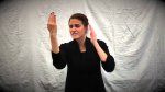 A woman telling a story in sign language, standing in front of a white fabric backdrop.