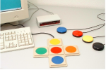 A computer screen and keyboard alongside a white console and several adapted switches.