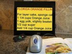 Gray kitchen mouse hovering over cookbook with black display screen mounted against wall showing magnified recipe text.