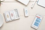 An iPhone with an audio transcription displayed. Next to the phone, there are four wearable microphones, which are long, white, and oval/rectangular, and have colored ovals in the center.