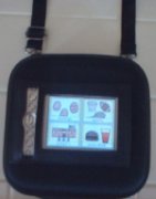 Small black square electronic device attached to a neck strap with a display showing a grid of four images.